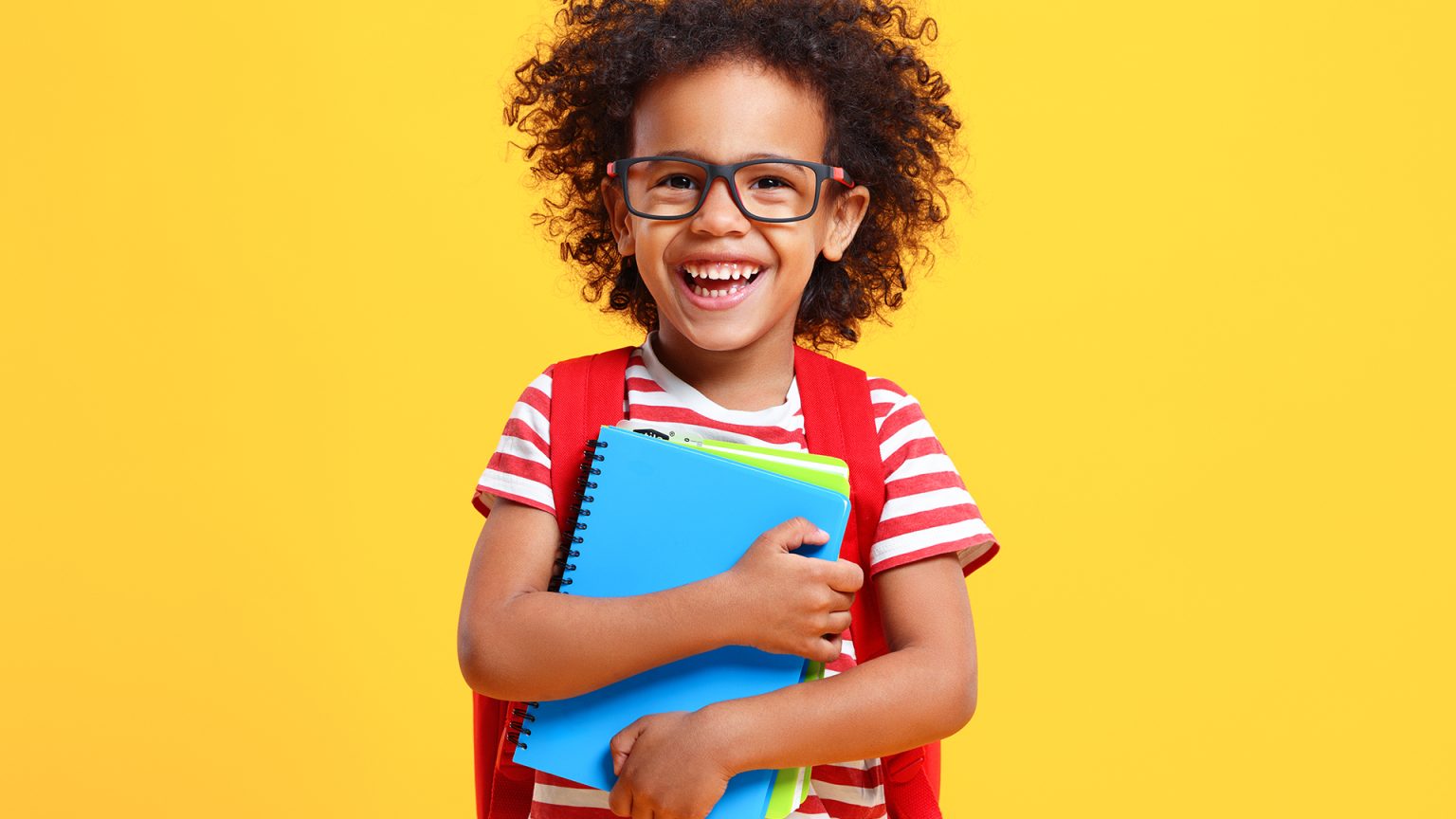 A happy schoolkid laughs at camera standing in studio with copybooks in hands.