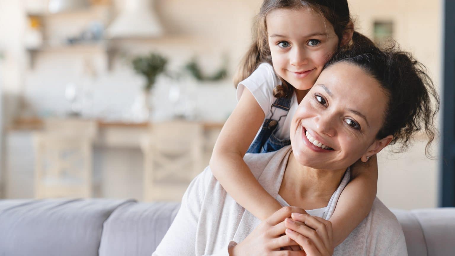 Happy Caucasian mother and cute little daughter girl hugging embracing , spending time together looking at camera at home.