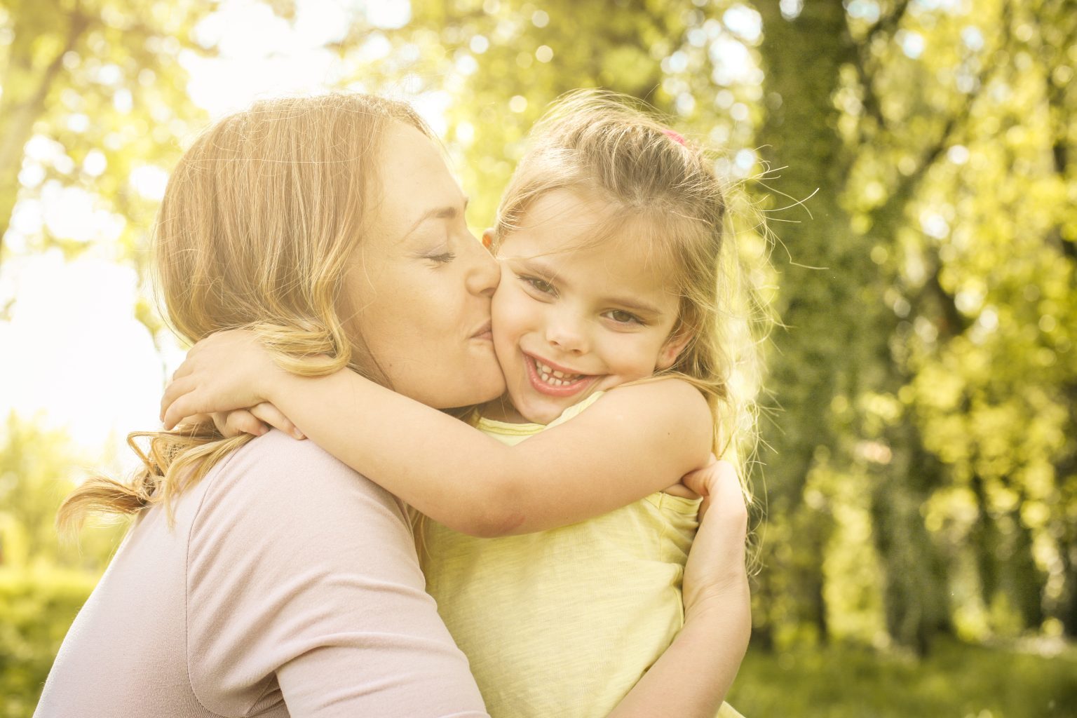 Mother and daughter outdoors in a meadow. Mother hugging and kissing her daughter in the meadow.