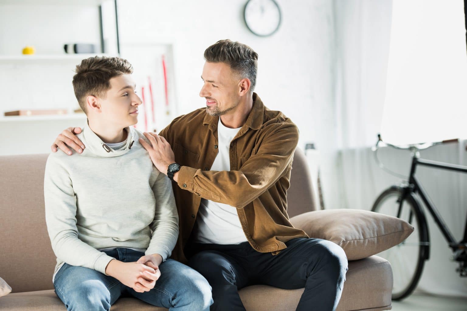 father hugging teen son on sofa at home