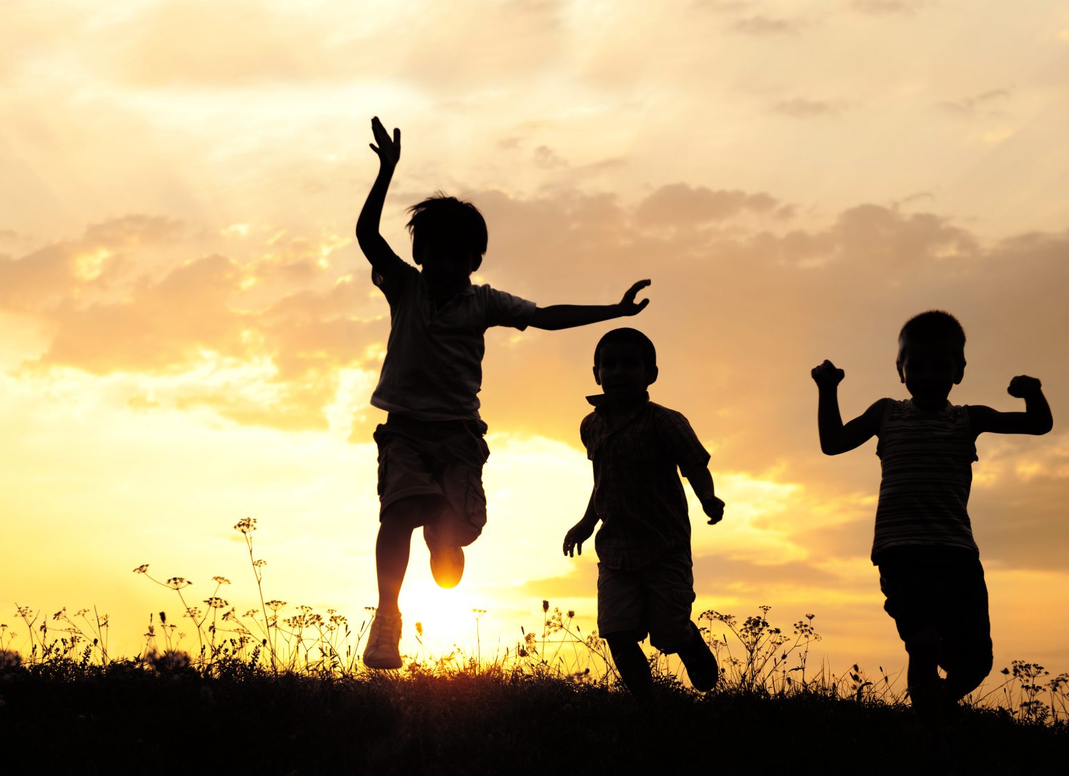 Three children running on meadow at sunset