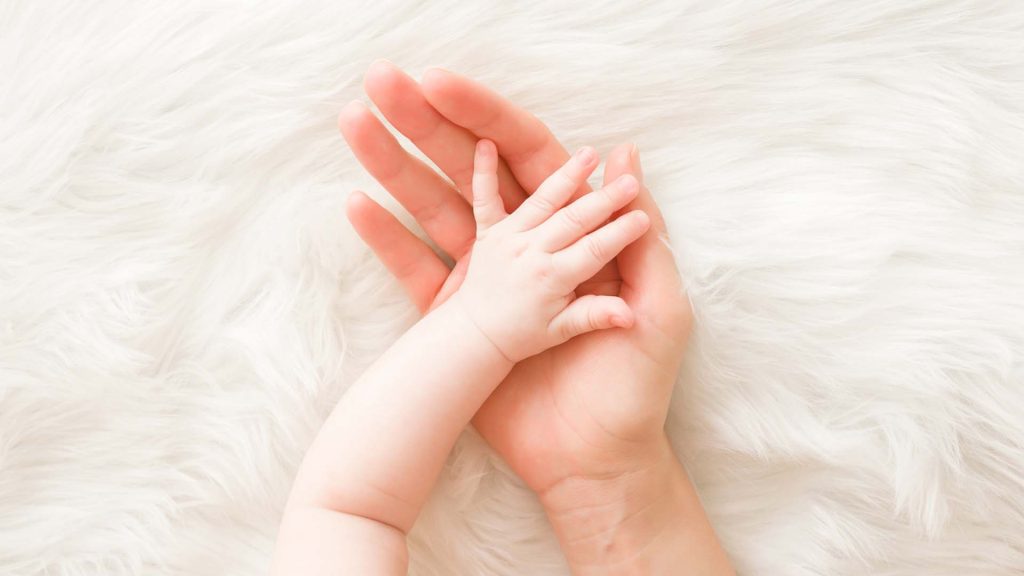 Infant hand on mothers palm on white fluffy furry background.