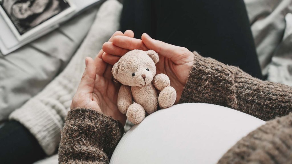 woman pregnant belly with little teddy bear