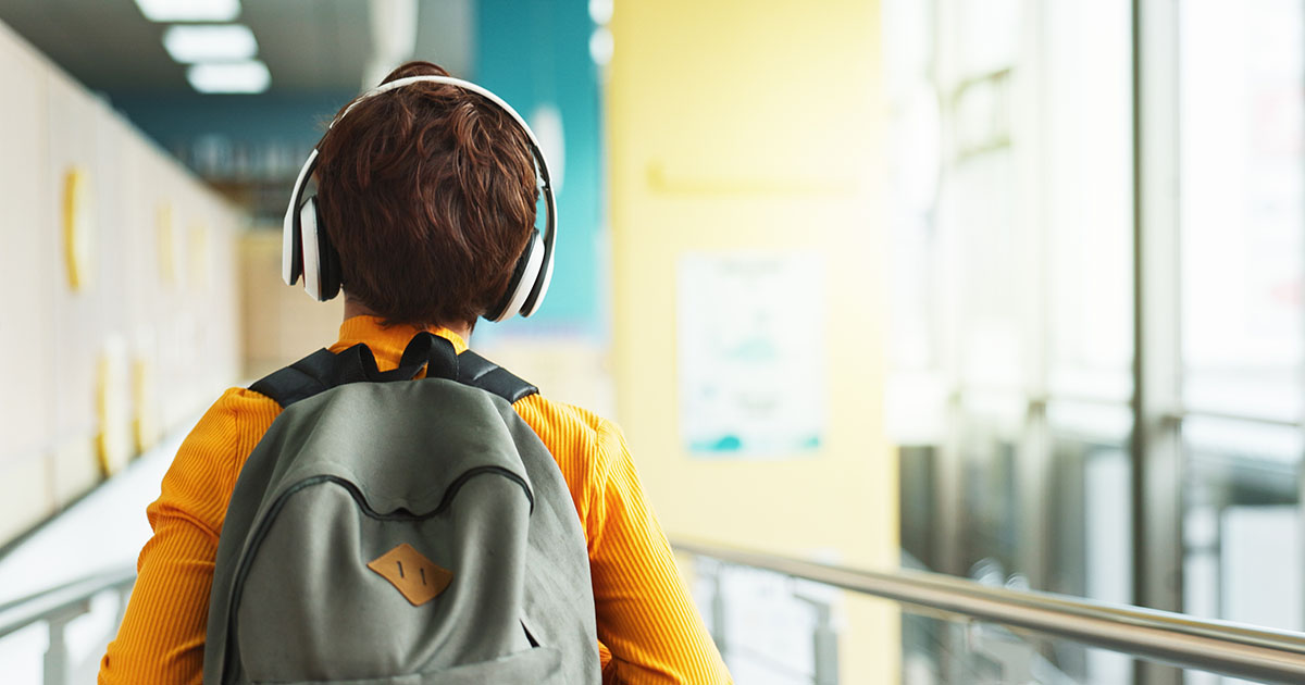 student walking in to school wearing a backpack and headphones.